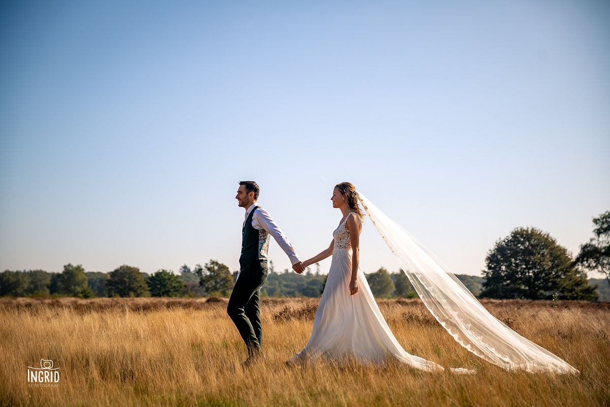 Bruid en bruidegom lopen door een kaal veld tijdens fotoshoot Ermelo