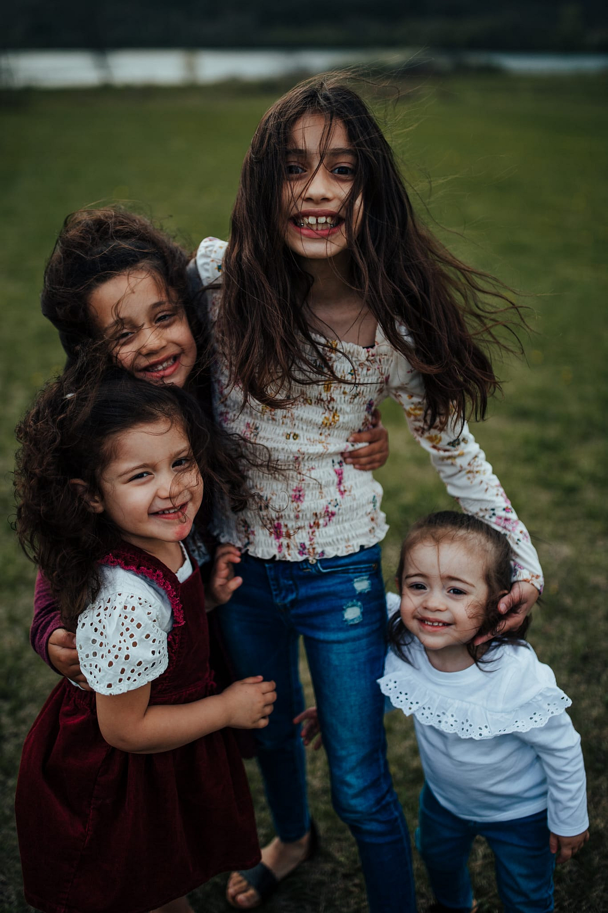 Four young girls stand together smiling as their hair whips in the wind.